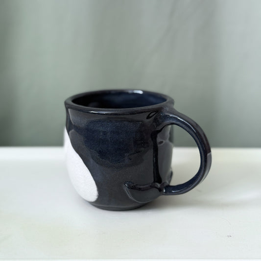 Black ceramic mug on a white surface with a gray background