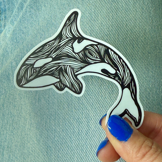 Hand holding a black and white stylized orca whale sticker on denim fabric