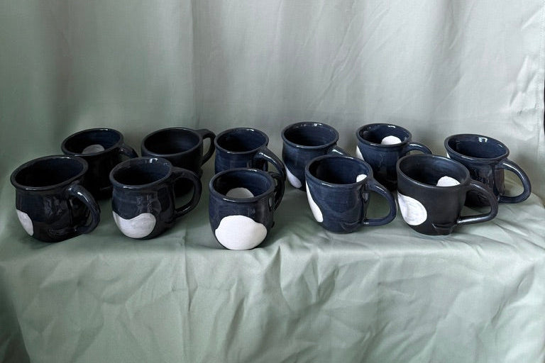 Set of black ceramic orca mugs with white accents on a light green fabric background