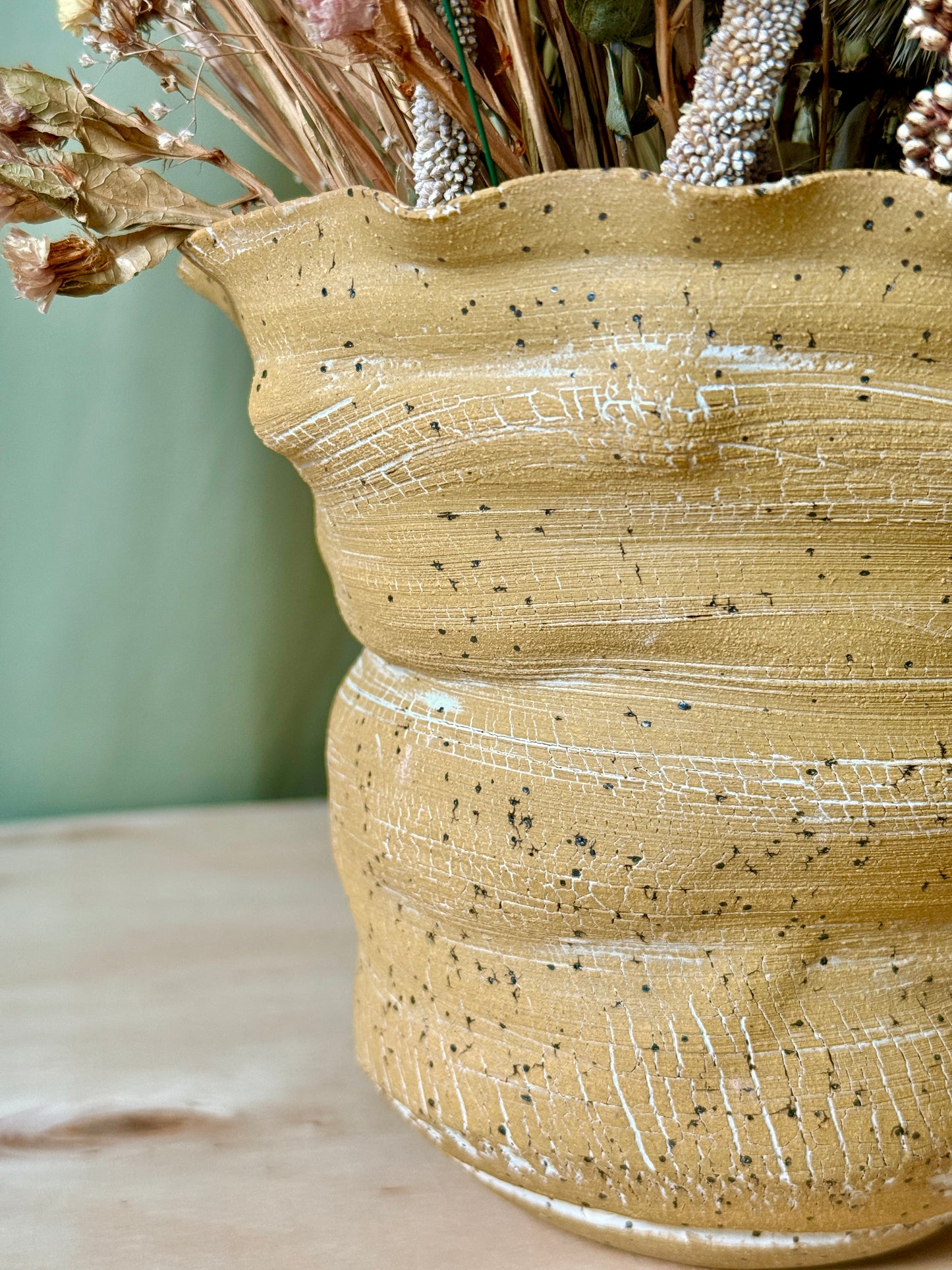 Textured ceramic vase with dried flowers on a light surface
