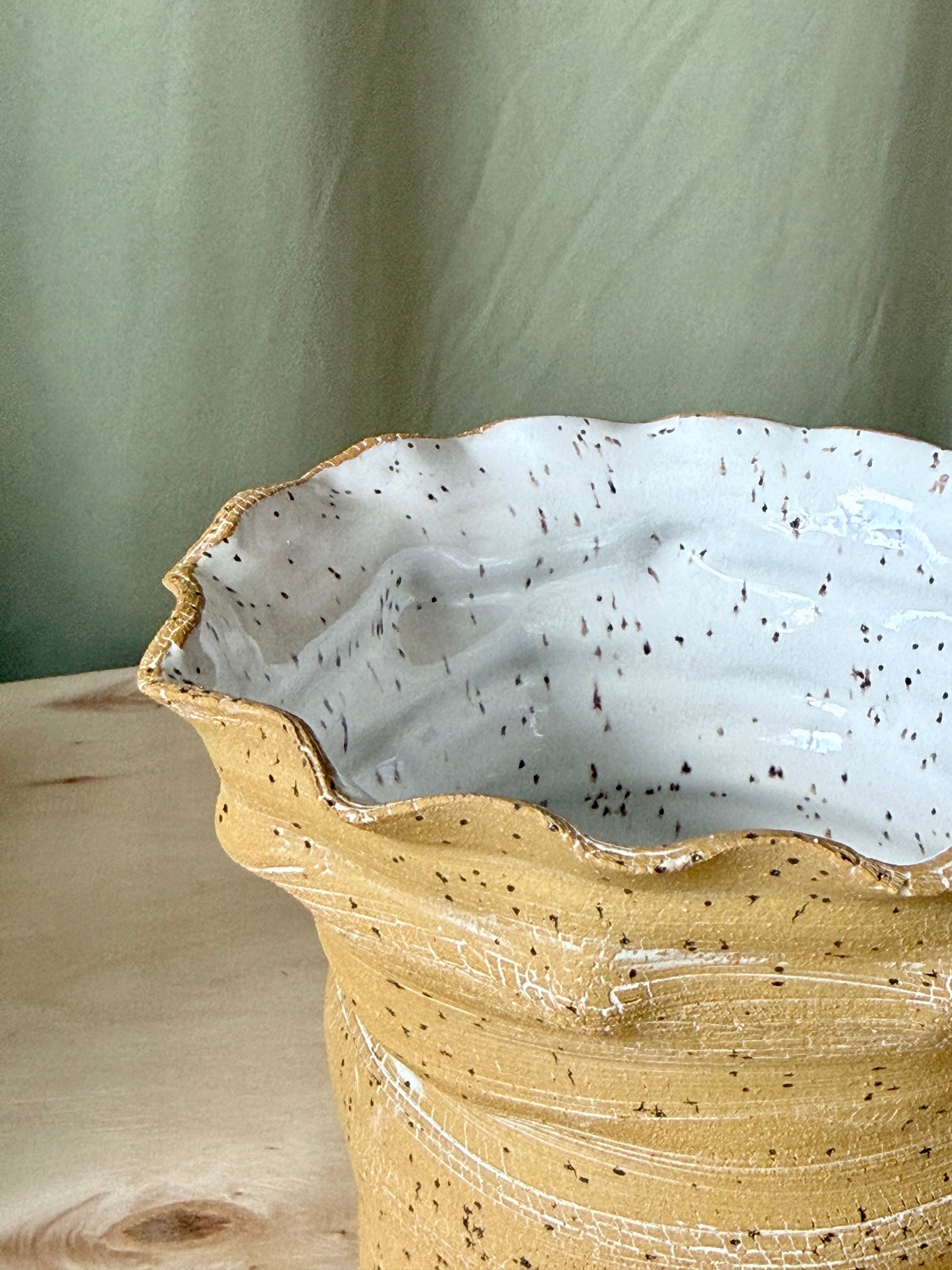 Ceramic vase with textured gold exterior and white interior on a wooden surface.