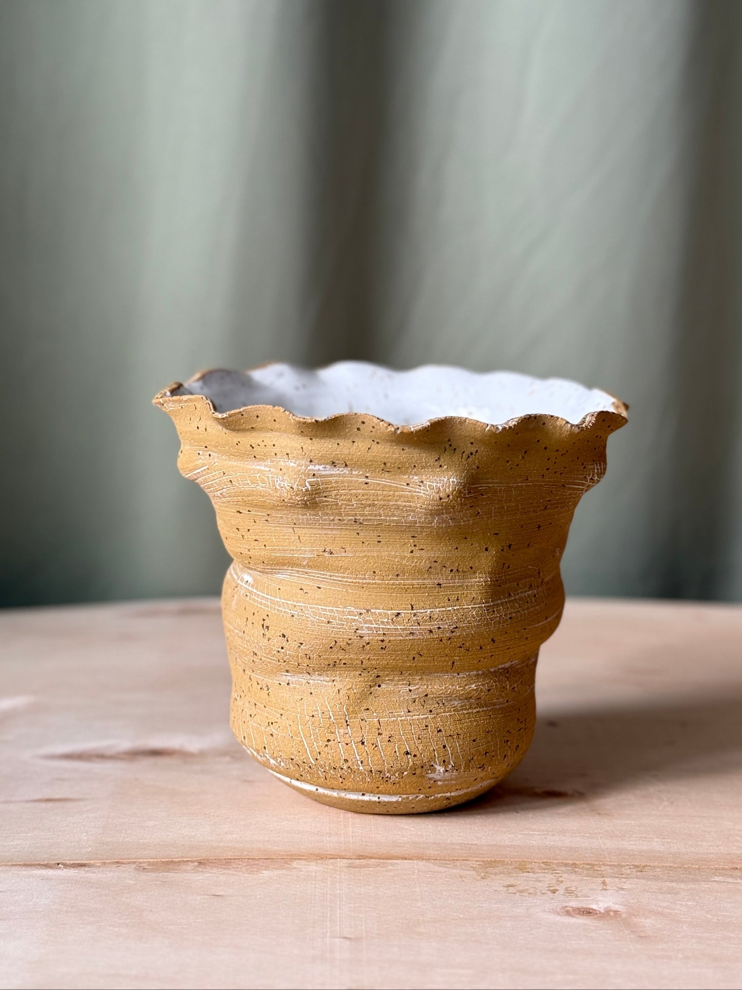 Ceramic vase with textured surface on a wooden table against a gray curtain background
