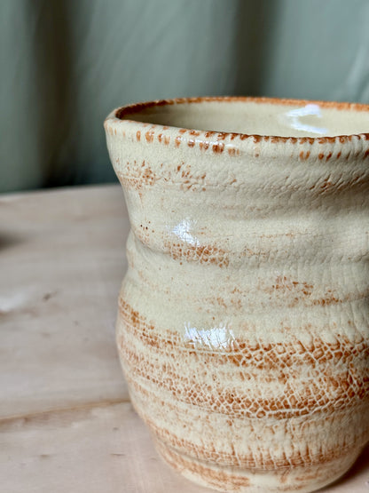 Close-up of a ceramic vase with brown speckles on a wooden surface.