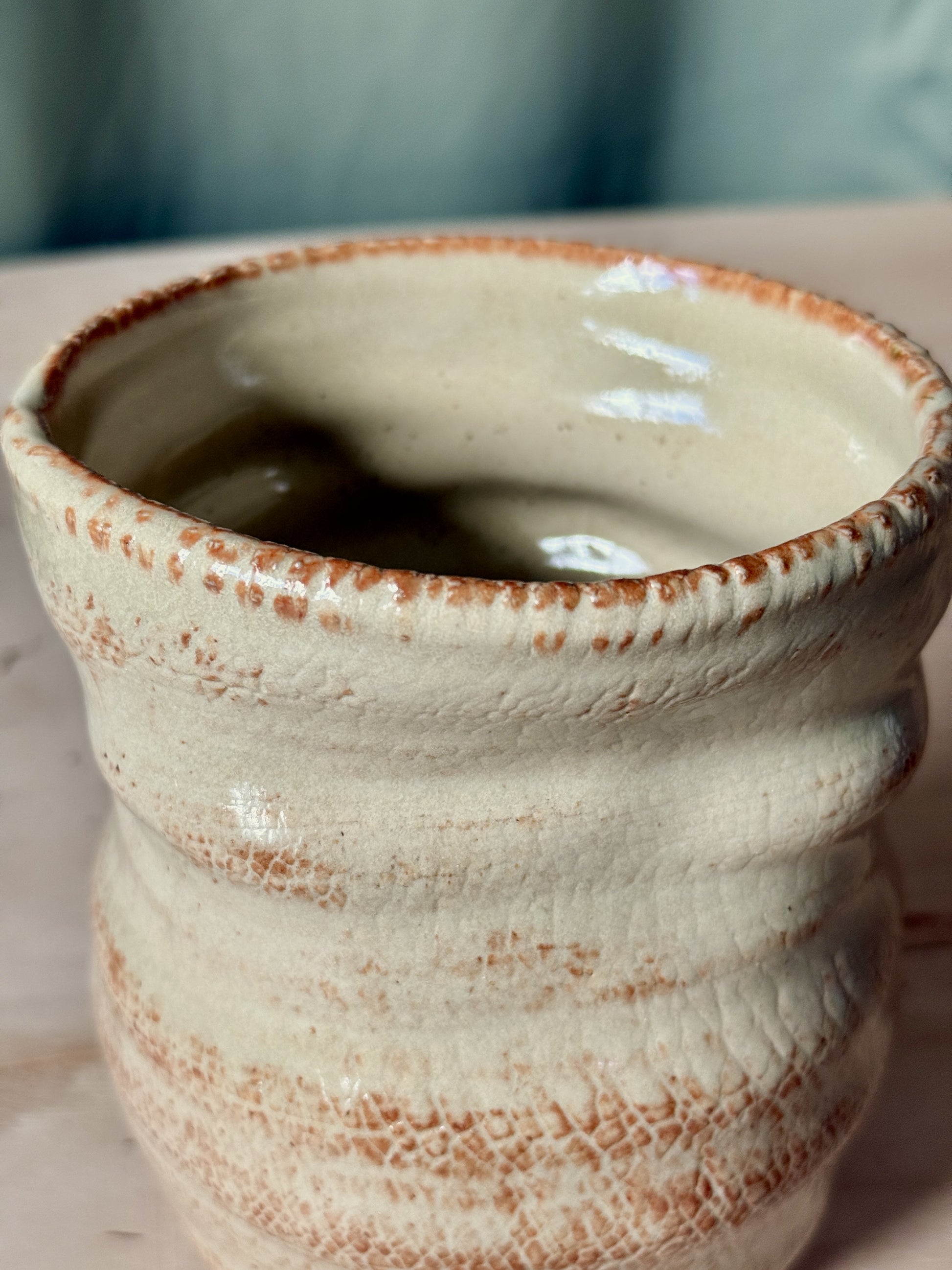Close up of a ceramic vase with a textured surface and brown rim on a light background