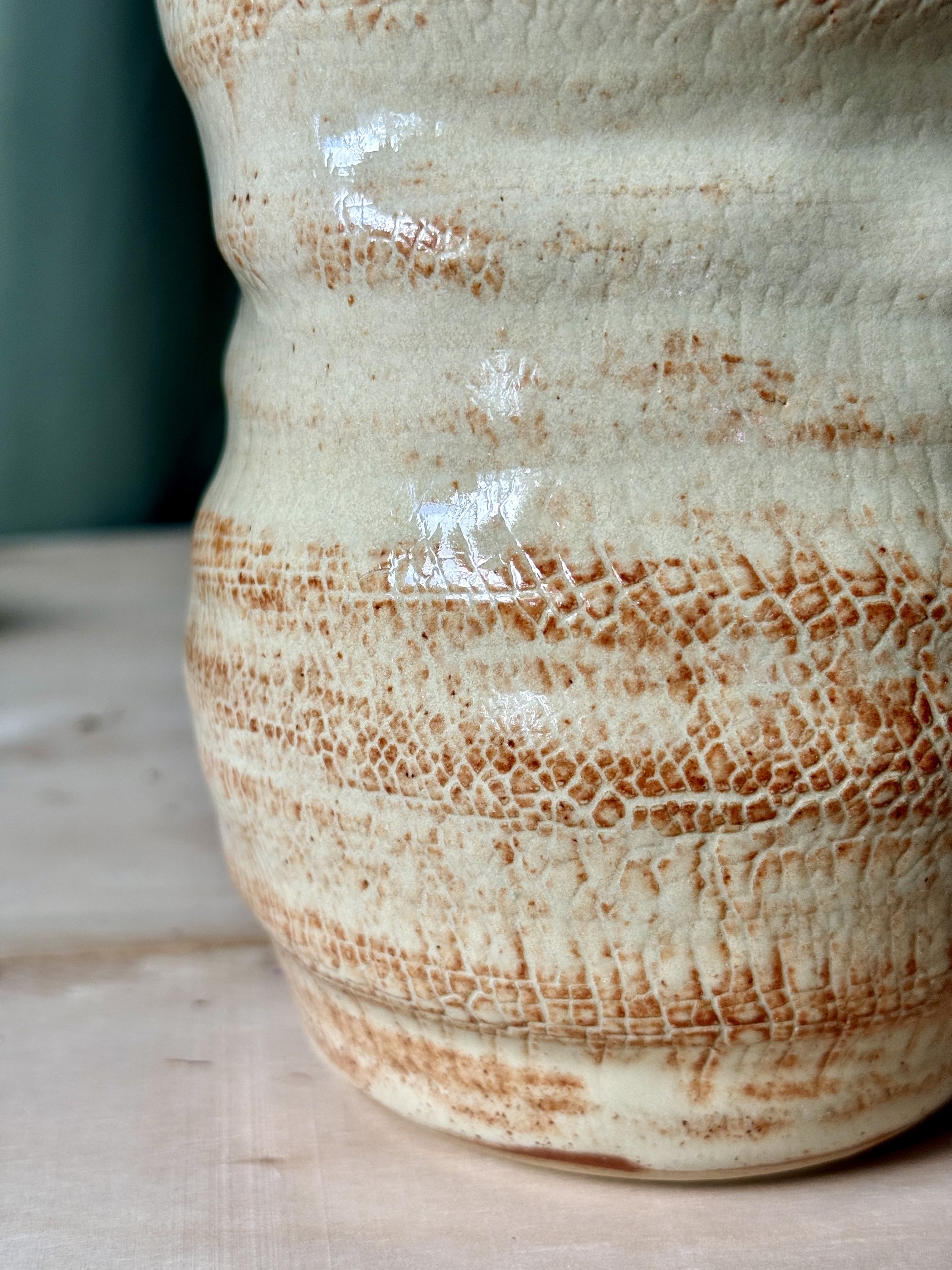 Close-up of a ceramic vase with brown speckled glaze on a wooden surface.
