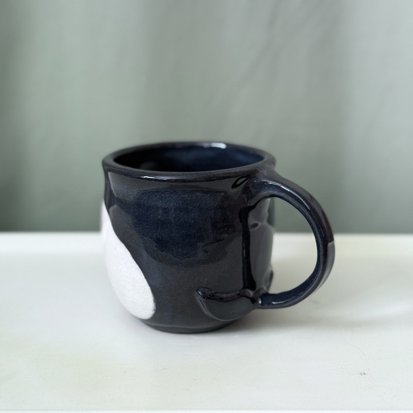 Black ceramic mug on a white surface with a gray background