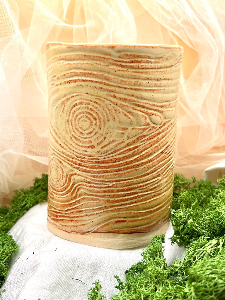 Cylindrical ceramic pot with wood grain texture on a white surface with greenery