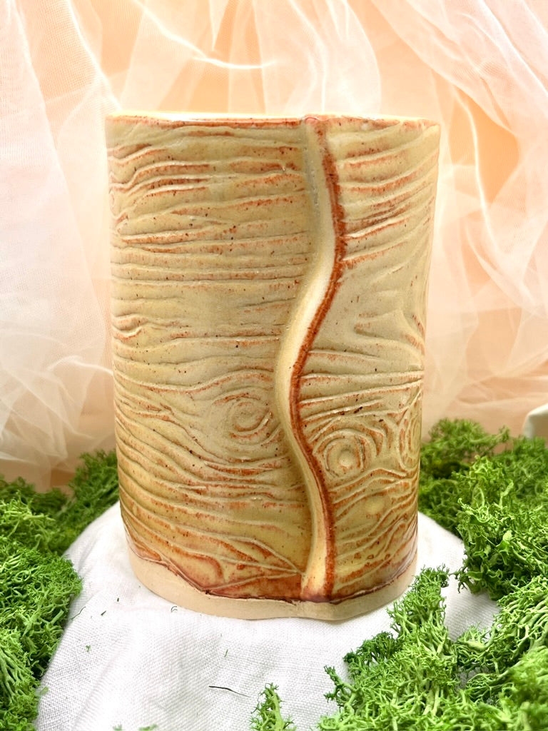 Cylindrical ceramic vase with textured design on a green grass-like surface
