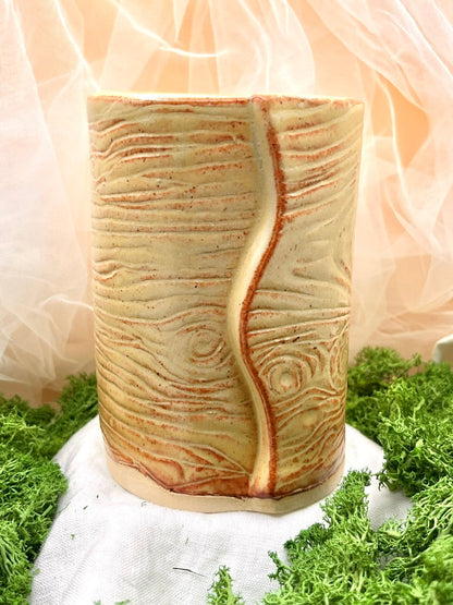 Cylindrical ceramic vase with textured design on a green grass-like surface